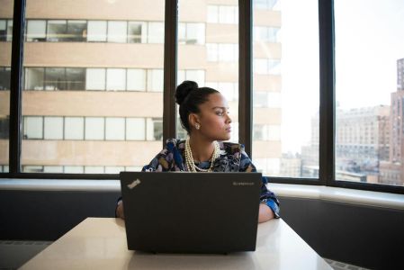 schwarze Dame sitzt vor Laptop an Schreibtisch und blickt seitlich