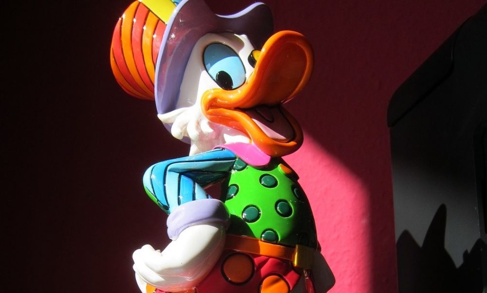 Dagobert Duck als Plastikfigur steht triumphierend auf einem Geldsack